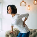 Image of a woman holding her lower back in discomfort, highlighting Thai massage benefits, including effective back pain management and improved spinal health for enhanced mobility and comfort.