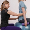 Image of a therapist guiding a woman sitting on an exercise ball, highlighting Thai massage benefits, including better posture and alignment for improved spinal health and physical balance.