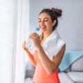 Image of a smiling woman holding a water bottle with a towel around her neck, highlighting Thai massage benefits, including increased energy levels, reduced fatigue, and enhanced vitality for an active lifestyle.