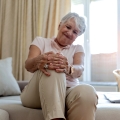 Image of a senior woman gently holding her knee, highlighting Thai massage benefits, including relief from osteoarthritis symptoms, improved joint flexibility, and enhanced quality of life.