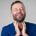 Image of a smiling man massaging his neck, highlighting Thai massage benefits, including relief from muscle tension and promoting relaxation for improved physical comfort.